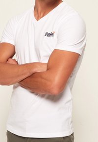 T-shirt blanc à manches courtes encolure en V, fabriqué en coton, avec un petit logo sur la zone de la poitrine gauche. Coupe slim avec une texture lisse.