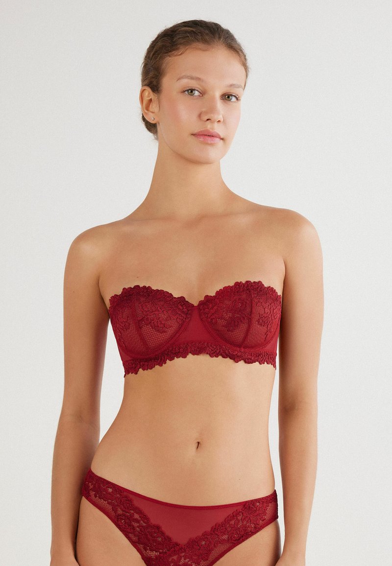 Rode kanten strapless beha met een gestructureerde basis en een bloemenpatroon, gecombineerd met een bijpassende transparante rode bikinibroekje, beide met ingewikkelde details.