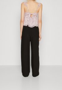 Ljusrosa blommig ärmlös topp med volangaxelband och knytning bak, kombinerad med löst sittande svarta byxor med vida ben.