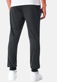 Schwarze Sporthose für Männer mit glattem Material, schlanker Passform und elastischen Knöchelbündchen, kombiniert mit weißen Sneakern.