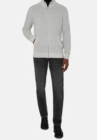 Grå zip-up cardigan med hög krage, ribbade muddar och fåll, samt sidofickor, kombinerad med mörka jeans och svarta sneakers.