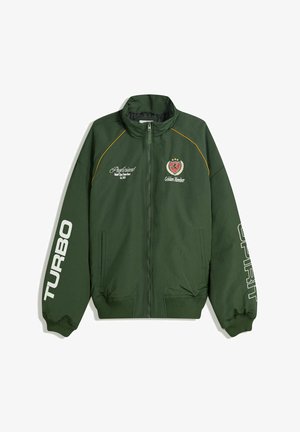 Grüne Bomberjacke mit Reißverschluss, gerippten Bündchen und Saum. Text auf den Ärmeln: "TURBO" und "SPIRIT." Logos auf der Brust in Gelb und Rot.