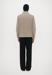 Beige long-sleeve shirt jacket with a collar, featuring a straight cut and buttoned cuffs, paired with black wide-leg trousers.