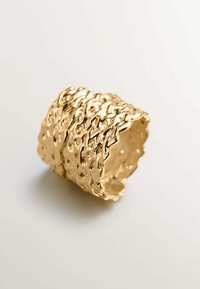Anillo tono dorado con un diseño entrelazado texturizado de forma ondulada y pequeños recortes a lo largo de los bordes, que demuestra una artesanía excepcional.