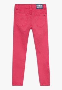 Jeans de denim rosa de Tommy Hilfiger con ajuste skinny, que cuentan con dos bolsillos traseros y una etiqueta de marca en la cinturilla. Textura suave, sin patrones visibles.