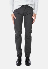 Pantaloni di cotone grigio scuro con un design a gamba dritta, abbinati a scarpe nere lucide. Il tessuto ha una superficie liscia senza motivi visibili.
