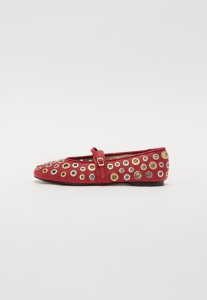 Red leather flat shoe with decorative metal eyelets in gold, silver, and black. Features a strap across the instep and rounded toe design.