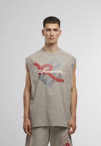 Beige sleeveless shirt with a large red and gray graphic design and white "Rocawear" text. Made from soft, lightweight fabric.