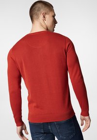 Czerwony sweter wykonany na drutach z okrągłym dekoltem, ściągaczami na mankietach i u dołu. Posiada gładką strukturę i dopasowany krój.