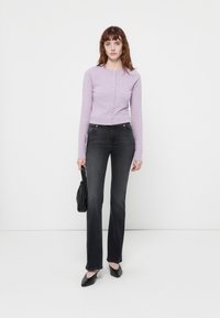 Cárdigan de punto de color púrpura claro con cuello redondo y cierre de botones, combinado con jeans acampanados oscuros y bailarinas negras de punta. Bolso negro.