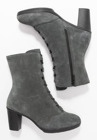 Stivaletti alla caviglia in suede grigio con tacco spesso nero, dotati di una cerniera laterale e un dettaglio di lacci decorativi. Texture liscia e design moderno.