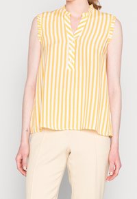 Blusa senza maniche a righe verticali gialle e bianche, con colletto alla cinese, maniche arricciate e una piaghetta con bottoni sul collo.