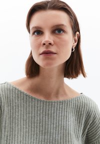 Ljusgrön ribbad stickad tröja med båthals, mjuk textur och enfärgad; modellen har en diskret silverfärgad hoopörhänge.