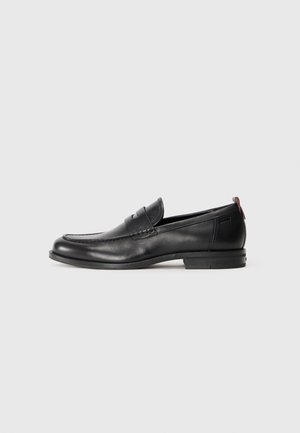 Zwarte leren loafers met een ronde neus, gestikte details en een kleine rode accent aan de hak. Laag- profiel rubberen zool.