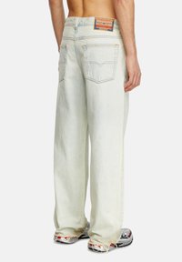 Jean en denim bleu clair, baggy, taille haute, avec poches arrière, patch de marque orange et détails à ourlet effiloché.