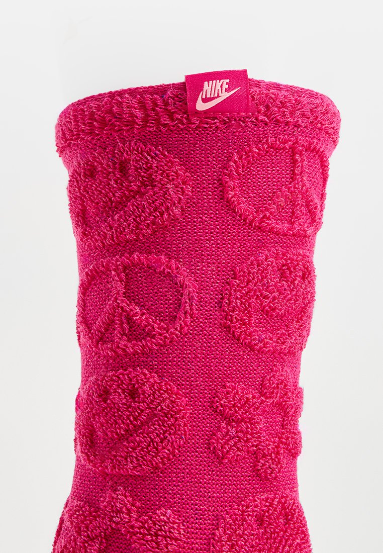 Helle pinke gestrickte Socke mit erhöhten Friedenstrukturen und blumigen Formen. Das obere Band ist gerippt und hat ein kleines Nike-Label auf der Vorderseite.