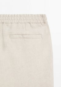 Close-up of beige fabric pants with an elastic waistband and a single horizontal back pocket without a visible closure.