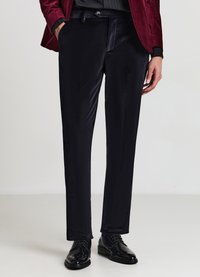 Schwarze Samthosen mit maßgeschneiderter Passform, glatttexturiert, mit Seitentaschen und dezentem Glanz, kombiniert mit schwarzen glänzenden Dressschuhen.