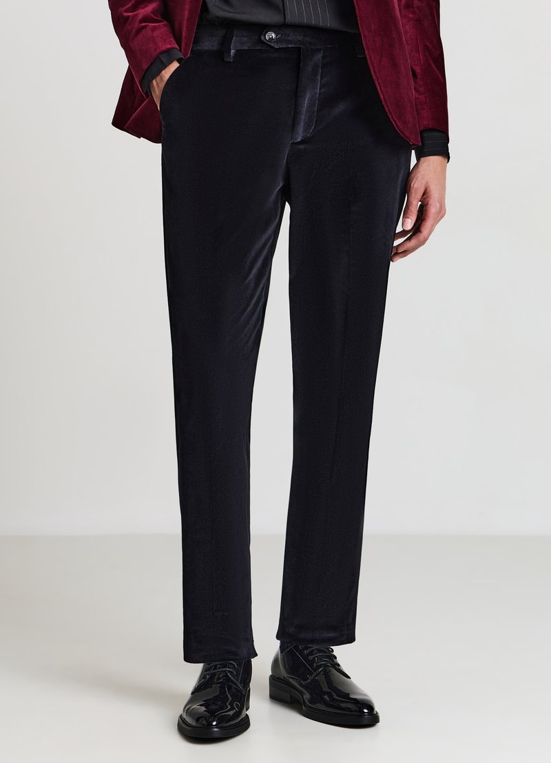 Schwarze Samthosen mit maßgeschneiderter Passform, glatttexturiert, mit Seitentaschen und dezentem Glanz, kombiniert mit schwarzen glänzenden Dressschuhen.