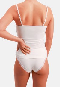 Hvid camisole med tynde stropper, kombineret med hvide trusser med lav talje og blonderkant. Glat tekstur med en tætsiddende pasform.