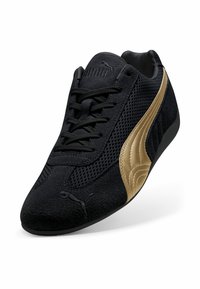 Sneaker nera con materiale scamosciato e in rete, caratterizzata da un logo PUMA dorato e dettagli in oro. Punta arrotondata e chiusura con lacci.