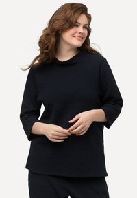 T unica blu navy con un motivo testurizzato, caratterizzata da un collo a imbuto e maniche a tre quarti, realizzata in un tessuto morbido.