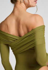 Olijf groene bodysuit met geplooide stofdesign, off-shoulder mouwen en een gladde textuur. Heeft een getailleerd silhouet en medium dekking.