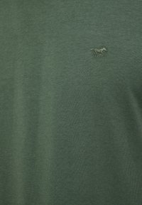 Ciemnozielona koszulka z miękkiej bawełnianej tkaniny, z małym haftowanym logo konia. Projekt jest prosty, bez widocznych wzorów.