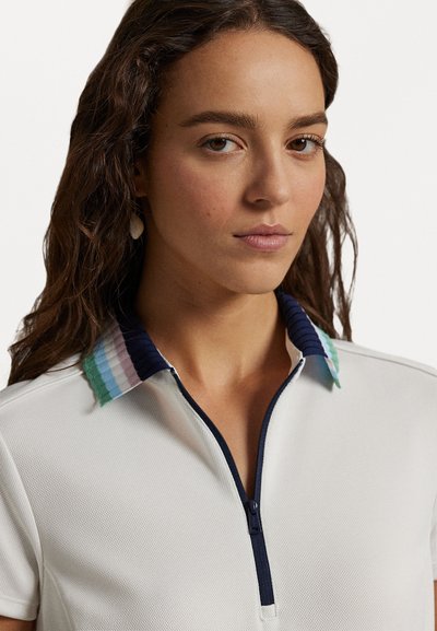 Bala polo krekls ar teksturētu audumu, ar tumši zilu rāvējslēdzēju un daudzkrāsainu svītrotu apkakli pasteļu toņos.