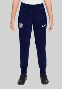 Marineblauwe sweatpants met een elastische tailleband, een witte Nike swoosh en een rond wit logo op het linkerbeen. Zacht materiaal met taps toelopende manchetten.