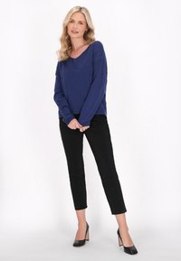 Tummansininen, pitkähihainen neule V-päällä, yhdistettynä mustiin slim-fit-housuihin ja mustiin korkokenkiin. Suora kangaslaatu.