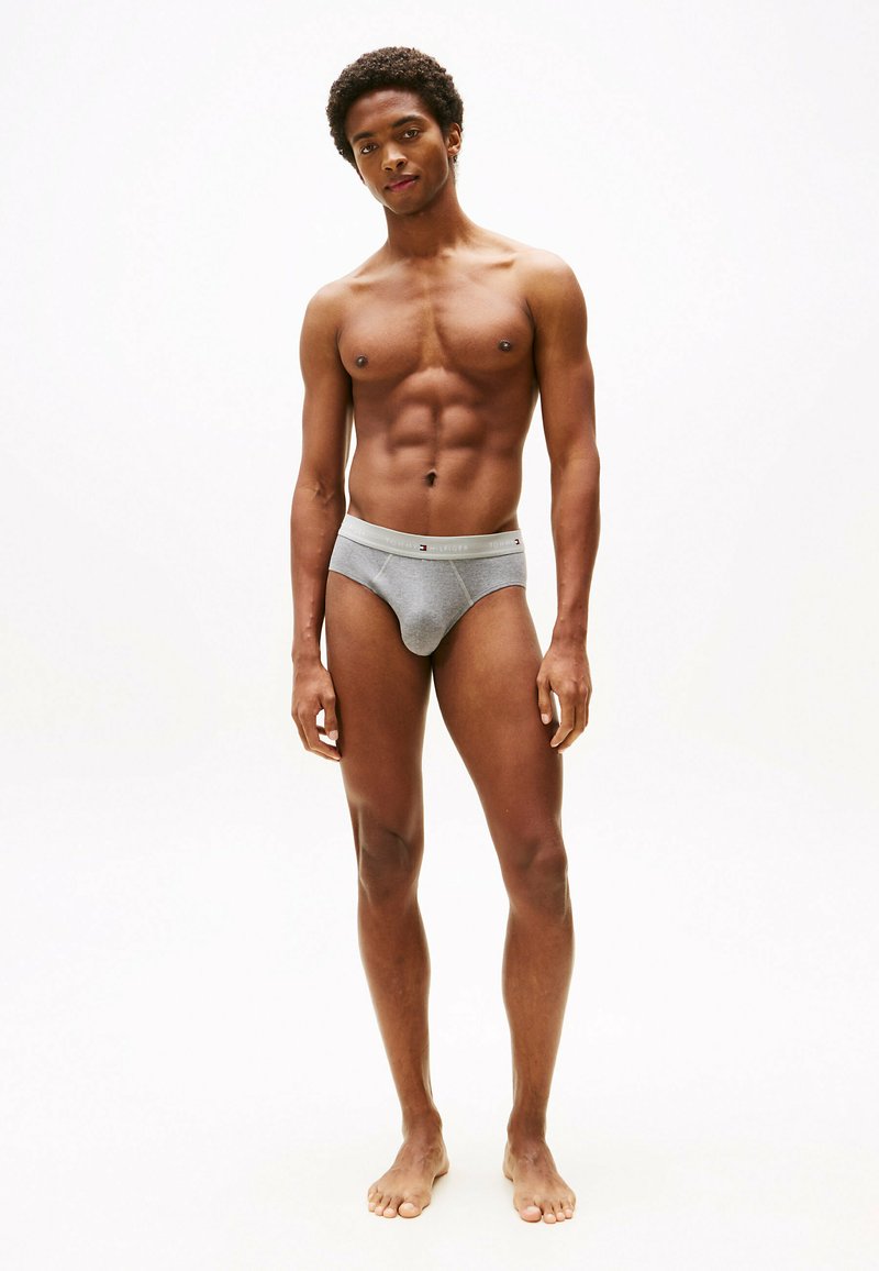 Caleçons en coton gris avec une ceinture élastique de marque, offrant un ajustement confortable et une texture lisse, portés par une silhouette masculine debout sur un fond neutre.