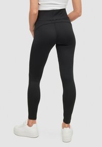 Leggings negros de cintura alta hechos de material elástico, con una textura suave y costuras laterales. Combinados con zapatillas deportivas blancas.