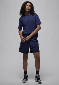 T-shirt atlético azul marinho com um pequeno logotipo branco, calções azul marinho a condizer e sapatilhas atléticas pretas com detalhes e logótipo brancos.