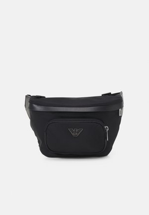 Sac banane noir avec poche zippée à l'avant et logo métallique Emporio Armani centré sur la poche, bandoulière réglable visible sur les côtés.