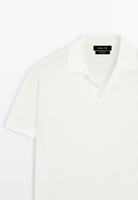 Polo shirt a maniche corte in cotone bianco testurizzato, con colletto classico e etichetta sul colletto. Design pulito e minimalista.