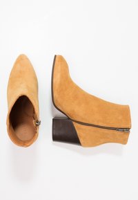 Botas de tobillo de ante color marrón claro con punta afilada y cremallera lateral. Tacón bloque y textura suave, con un tacón de madera marrón.