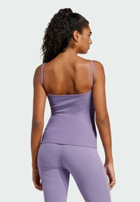 Svetlofialová tielko s tenkými ramienkami, priliehavý strih, ryhovaná textúra a nízky chrbát. Skombinované s ladnými fialovými legínami.