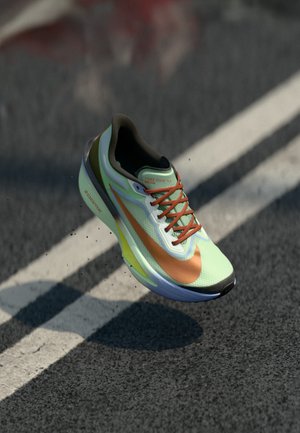 Pantof sport Nike Zoom Fly verde deschis și portocaliu plutind deasupra unui drum asfaltat cu marcaje albe de benzi.