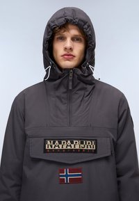 Grijze waterdichte jack met een voorzak, trekkoord capuchon en een patch met de vlag van Noorwegen. Inclusief merklogo op de borst.