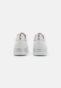 Witte sneaker met een gladde leren bovenkant, metallic zilveren accenten op de hiel en een gestructureerde rubberen zool met een gelaagd ontwerp.