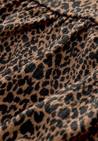 Tkanina s leopardím vzorem s béžovým pozadím a černými skvrnami, texturovaný povrch s pomačkaným vzhledem a jemným splývavým efektem.