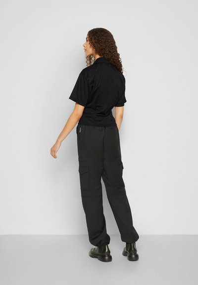 Camisa preta de manga curta com gola, combinada com calças cargo pretas folgadas com múltiplos bolsos e punhos ajustáveis.