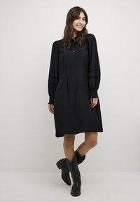 Zwarte jurk met een kraag, lange pofmouwen en decoratieve strepen. Heeft een comfortabele pasvorm en subtiele plooien bij de taille.