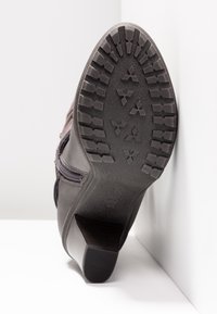 Bottine en cuir noir avec une semelle en caoutchouc texturée, un motif de bande de roulement visible et un talon bloc. Comprend une fermeture éclair latérale pour un enfilage facile.
