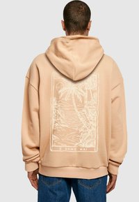 Ferskenfarvet hoodie med en kængurulomme og et stort hvidt grafisk motiv af palmer og en solnedgang på ryggen. Blødt, struktureret stof.