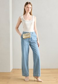 White ribbed tank top with black trim, light blue wide-leg jeans, and strappy beige heels; small gold-textured crossbody bag.