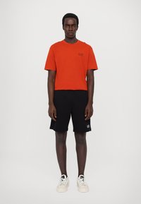 Tricou roșu cu mâneci scurte, cu logo-ul EA7, asortat cu pantaloni scurți negri și adidași albi. Design simplu, material din bumbac, croială lejeră.