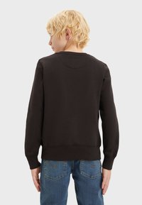 Sudadera negra con cuello redondo, puños y dobladillo acanalados. Presenta una textura suave y un diseño liso, combinada con jeans de mezclilla azules.