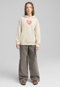 Sudadera crema con un gráfico de corazón de llamas rosas, combinada con pantalones grises holgados y zapatos marrones sin cordones. Fondo neutro.